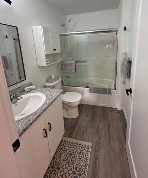 A modern bathroom with a glass-enclosed shower, a white sink, a toilet, and a mirror.