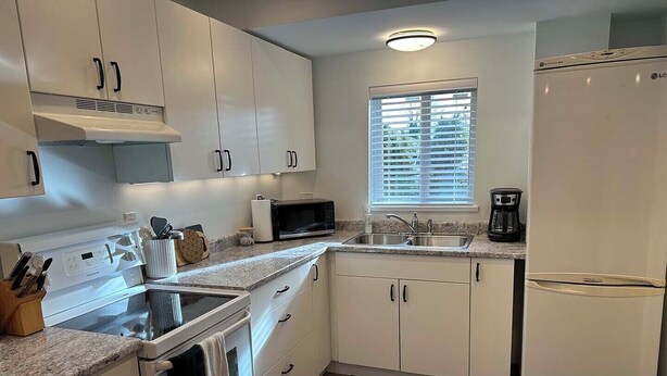 A modern kitchen with white cabinets, a built-in oven, a microwave, a coffee maker, and a window with blinds. - Private suite steps away from the ferry and some of Powell River's best dining. (Powell River)