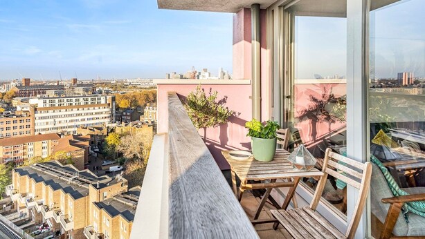 A balcony with a table and chairs, a potted plant, and a view of the cityscape.