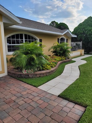 A residential house with a paved driveway, a stone border garden, and a well-maintained lawn. - Cozy 2 Bedroom Sebring Garden Retreat ~ Private Entrance ~ AC and Wi-Fi (Sebring)