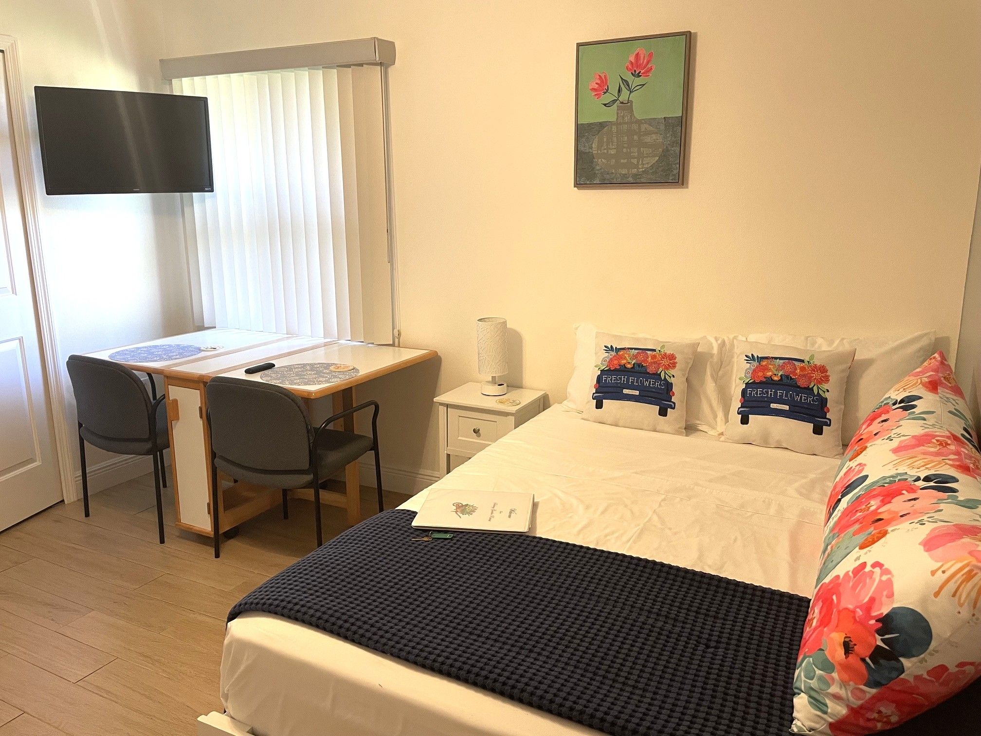 Ein Schlafzimmer mit Bett, Kissen, Schreibtisch, Stuhl, Nachttisch und einem an der Wand befestigten Fernseher.