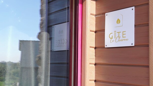 Ein Gebäude mit Holzfassade und einem Schild, auf dem 'GITE Le Charme' steht.