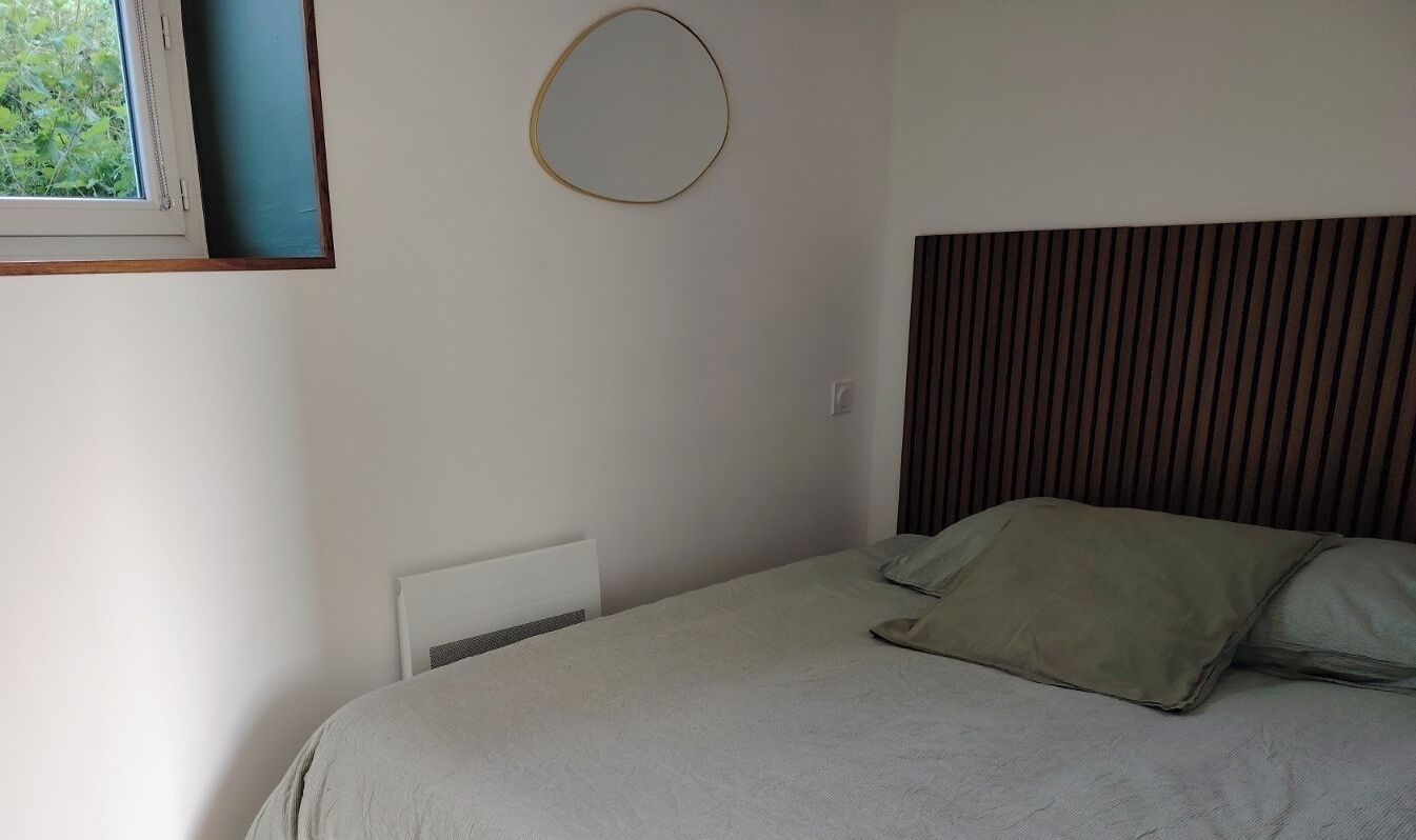 Une chambre à coucher avec un lit, une fenêtre, un radiateur et un miroir fixé au mur.