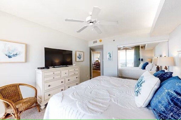 A hotel room with a large bed, a television on a dresser, a ceiling fan, and a mirror. - Great Fall & Winter Rates; Refreshed Ground Floor Unit Steps to Beach and Pool. (Orange Beach)