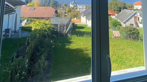 A view through a window of a residential area with houses, a grassy yard, and mountains in the background.