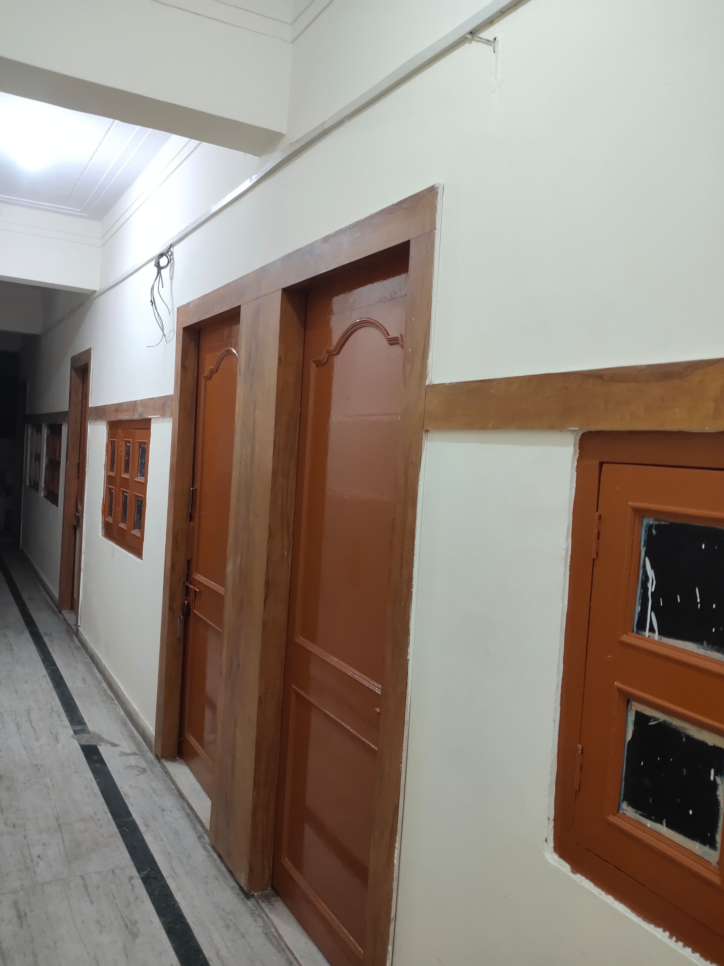 Un pasillo con puertas y ventanas de madera, paredes blancas y piso de baldosas.