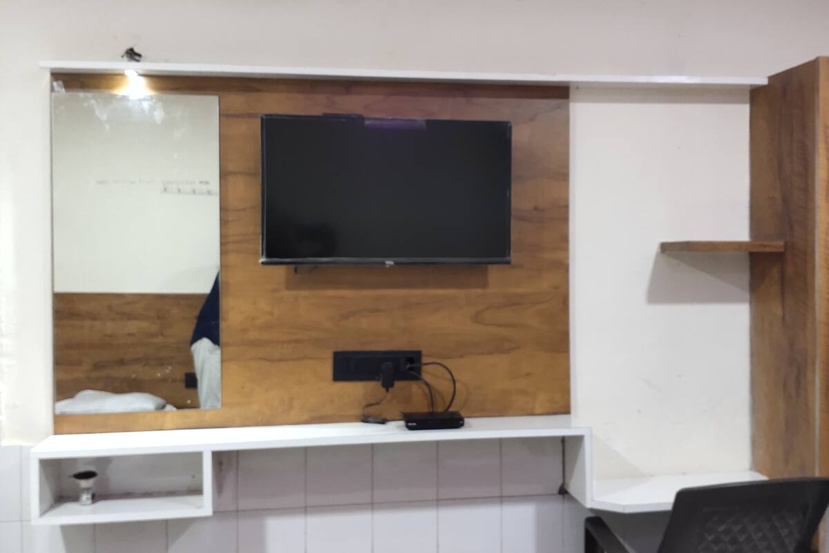 Quarto moderno com televisão na parede, painel de madeira, estantes brancas e uma mesa com cadeira.