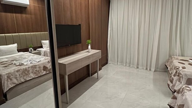 A modern hotel room with a large mirror, a flat-screen TV, a bedside table, and a bed with a patterned bedspread. - Royal Home Hotel (Cairo)
