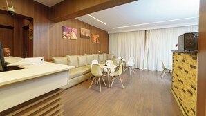 A hotel lobby with a reception desk, a sofa, a dining area, and a television. - Royal Home Hotel (Cairo)