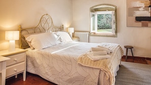 Una cama bien hecha con una colcha estampada, una lámpara de noche y una ventana con vistas a zonas verdes.