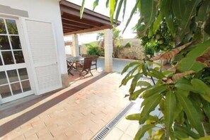 Relax in this serene outdoor space with a dining table and chairs, surrounded by lush greenery and a shaded pergola.
