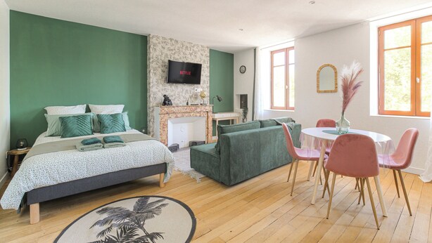 Une chambre à coucher avec un lit, un canapé vert, une table à manger avec des chaises, une cheminée et un téléviseur fixé au mur.