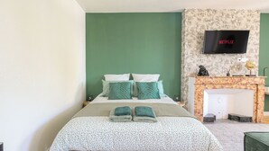 Une chambre à coucher avec un lit, des murs verts, une cheminée, un téléviseur et une petite table avec une lampe.