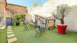 Une cour avec une pelouse artificielle, des sièges d’extérieur, des plantes en pot et un mur en pierre.