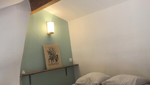 A single bed with a headboard, a wall-mounted light, a framed picture, and two pillows.