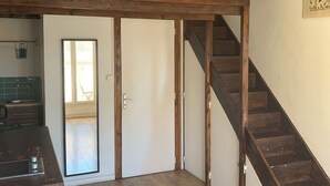A spacious loft with a wooden staircase, a kitchen area, and a view of the outdoors.