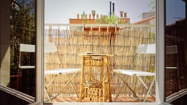 A view through a window of a room with a bamboo fence, two white chairs, and a small table.