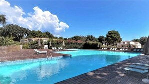 Une piscine entourée d’arbres et d’immeubles, avec des chaises longues et des parasols.