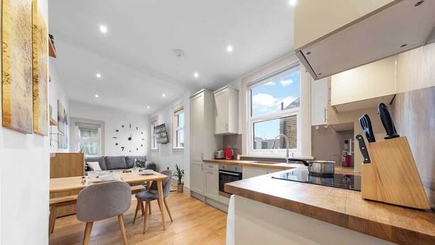 A modern kitchen with wooden countertops, a dining area with a table and chairs, and a large window providing natural light. - Modern Spacious 1 Bed Flat near Richmond Park and River Thames  (London)