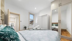 A bedroom with a large bed, a wardrobe, a window, and a view of the outside. - Modern Spacious 1 Bed Flat near Richmond Park and River Thames  (London)