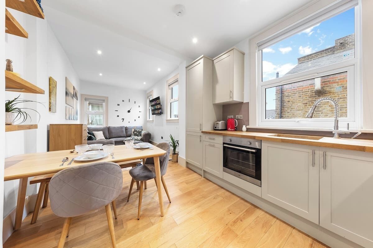 A modern kitchen with wooden flooring, white cabinets, and a large window.