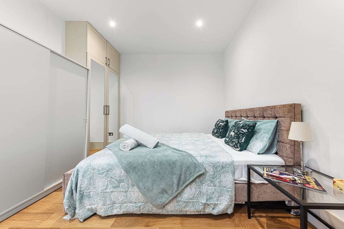 A bedroom with a bed, a bedside table, a lamp, and a wardrobe.