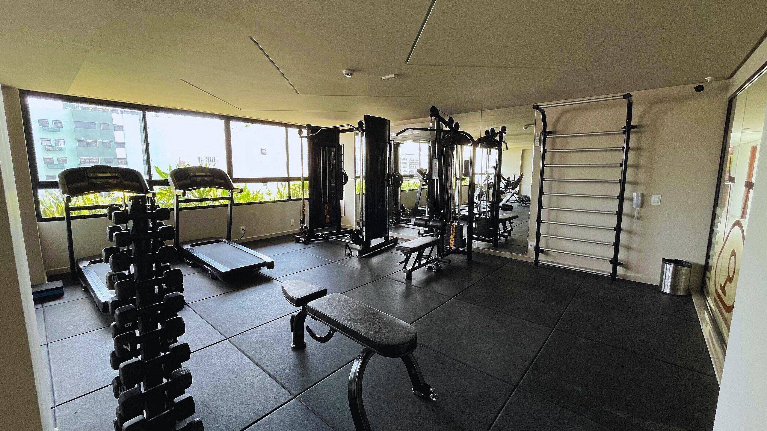 A gym with exercise equipment, a bench, and large windows.