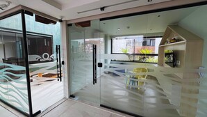A modern interior with a glass door leading to a seating area with chairs and a table. - Flat Oceânica Deluxe - By Almare (João Pessoa)