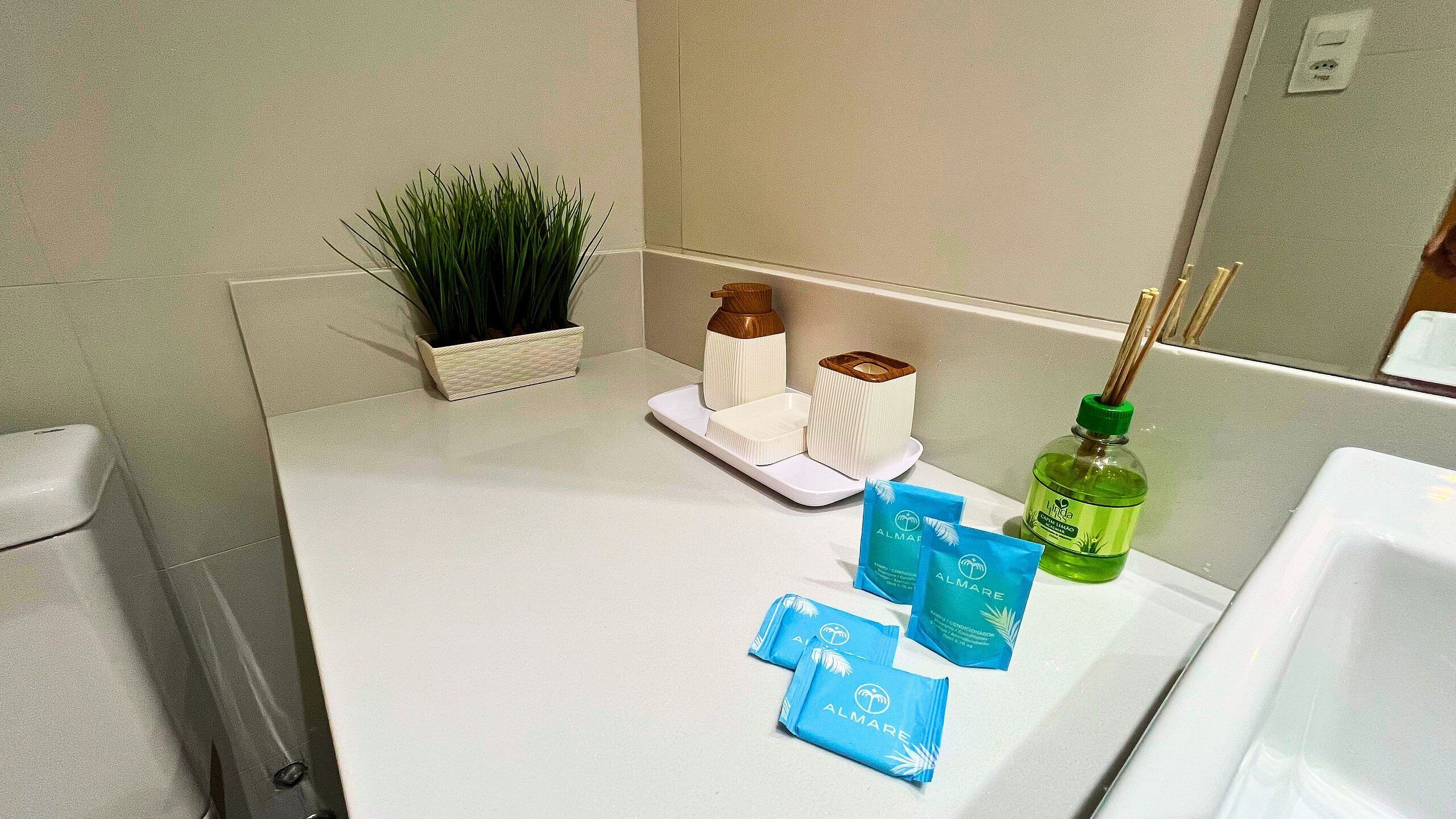 A bathroom counter with a plant, soap dispensers, a bottle of liquid soap, and two blue sachets of air freshener.