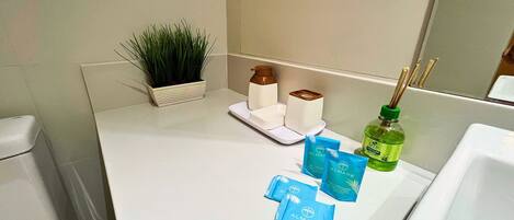 A bathroom counter with a plant, soap dispensers, a bottle of liquid soap, and two blue sachets of air freshener.