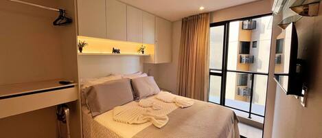A modern bedroom with a bed, a wardrobe, a mirror, and a window with a view of buildings.