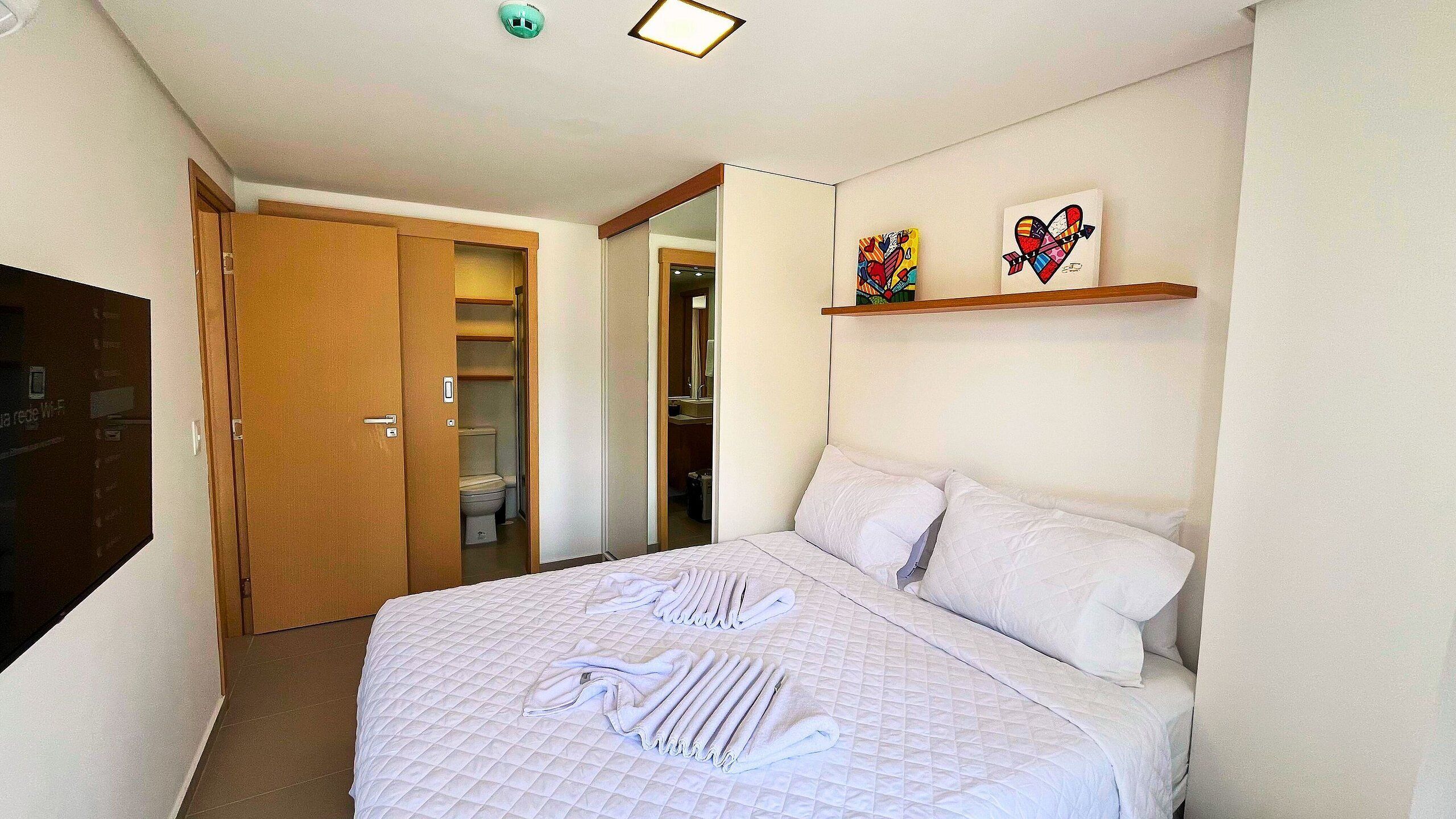 A hotel room with a bed, a wardrobe, a bathroom, and two artworks on the wall.