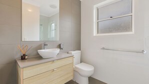 Un baño moderno con un lavamanos blanco, un espejo, un inodoro y una ventana.