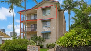 Un edificio de varios pisos llamado "Ocean Vista" con balcones, fachada de ladrillo y vegetación circundante.