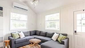Een moderne woonkamer met een grijze modulaire bank, twee kleine houten krukjes en een geweven poef.