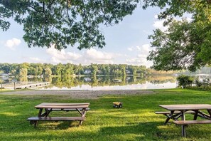 A lakeside picnic area with two picnic tables and a toy car on the grass.