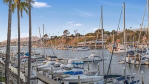 A marina with numerous boats docked, surrounded by palm trees and a hilly landscape in the background. - Serene Harborfront Condo | Unbeatable Views & Coastal Charm (Oceanside)