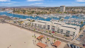 A marina with numerous boats docked, a beachfront hotel with multiple floors, and a clear view of the surrounding landscape. - Serene Harborfront Condo | Unbeatable Views & Coastal Charm (Oceanside)