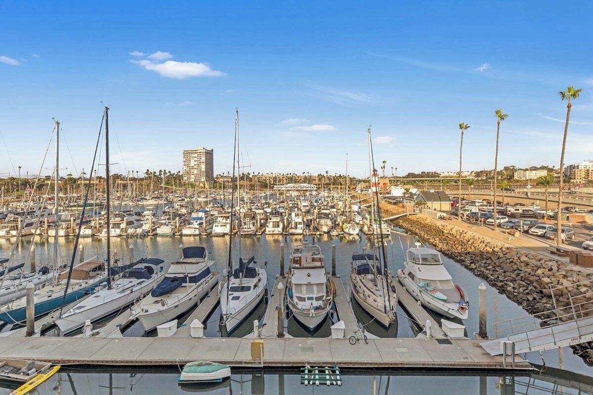 Uma marina com vários barcos atracados, céu claro e um edifício ao longe.
