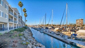 Un port de plaisance avec des bateaux amarrés le long d’un canal, un immeuble doté de balcons et un ciel dégagé.