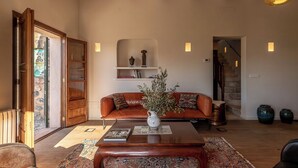 Ein gemütliches Wohnzimmer mit einem Holztisch, einer Couch mit Kissen, einer Vase mit Pflanzen und einer Treppe im Hintergrund.