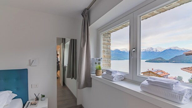 Ein Schlafzimmer mit Bett, Nachttisch, Fenster mit Blick auf Berge und einen See sowie einer Treppe, die in einen weiteren Raum führt.
