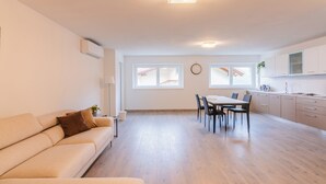 Ein modernes Wohnzimmer mit einer Couch, einem Esstisch und Stühlen. Es gibt eine Küchenzeile mit Schränken und einer Spüle.