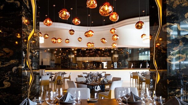 A restaurant with a modern interior, featuring a central bar area and multiple dining tables set for guests. - Hotel Mousai - 2 bedroom (Cancún)