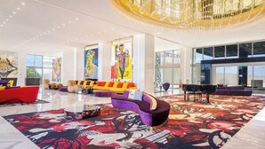 A spacious lobby with a modern chandelier, vibrant seating areas, and large windows. - Hotel Mousai - 2 bedroom (Cancún)