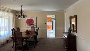 A dining room with a chandelier, a red floral painting, and a view into the kitchen.