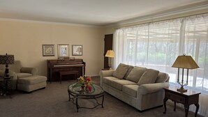 A living room with a piano, two armchairs, a glass coffee table with flowers, and a sofa.