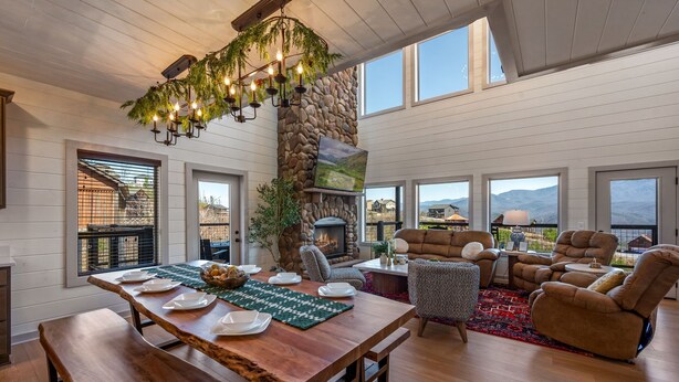 Amplia sala de estar con una gran mesa de madera dispuesta para comer, una chimenea de piedra y varias zonas de estar.