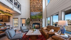 Amplia sala de estar con chimenea de piedra, asientos cómodos y ventanas grandes con vistas al exterior.