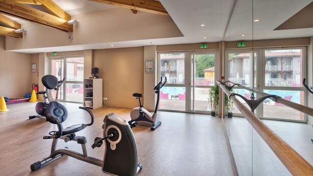 Un gimnasio con bicicletas estáticas y máquinas de cardio, vigas de madera en el techo y grandes ventanales con vistas al exterior.